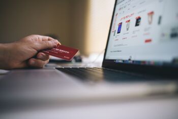 Eine Person shoppt am Laptop im Netz und hält eine Kreditkarte in der linken Hand
